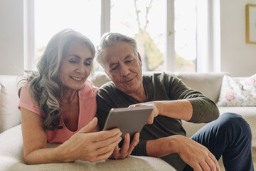 Happy senior couple relaxing on couch at home using tablet