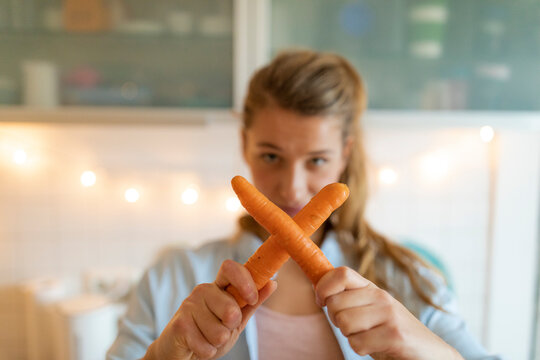 Young woman holding carrots at home