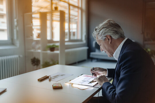 Senior businessman drawing on shining tablet