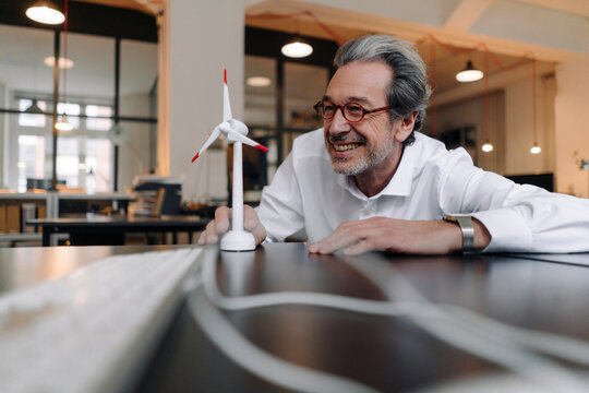 Happy senior businessman with wind turbine model in office