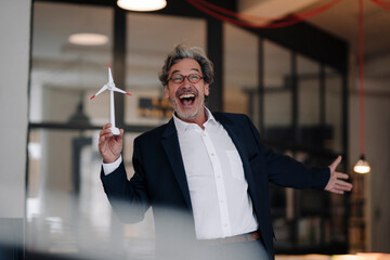 Excited senior businessman with wind turbine model in office
