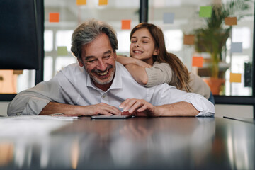 Happy senior buisinessman and girl looking at tablet in office