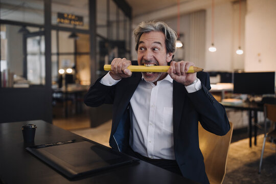Angry senior businessman with giant pencil at desk in office