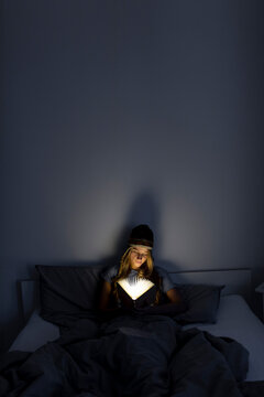 Young woman reading illuminated book in bed at home