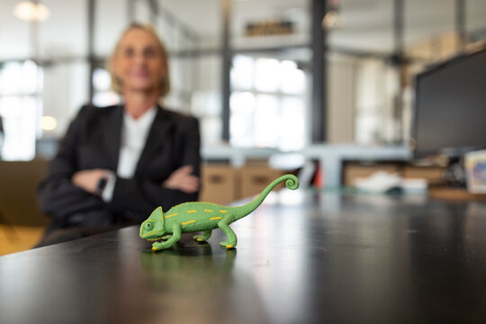 Mature businesswoman with chameleon figurine on desk in office