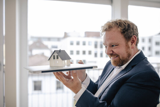 Smiling businessman holding model house in office
