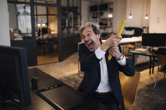 Angry senior businessman with giant pencil at desk in office