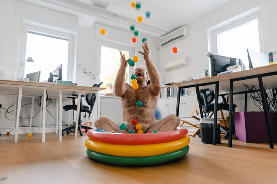 Crazy businessman sitting in wading pool in office playing with balls
