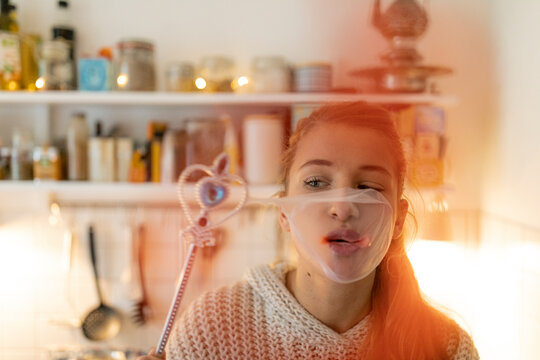 Young woman in kitchen at home with magic wand and burst chewing gum bubble
