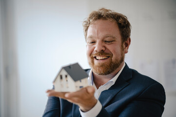 Happy businessman holding model house in office