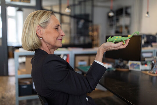Mature businesswoman holding chameleon figurine in office