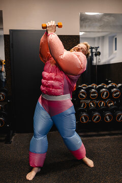 Man in gym wearing pink bodybuilder costume lifting dumbbell