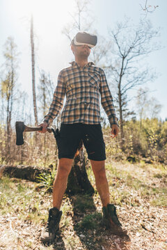 Young man gaming with VR glasses in the forest, holding axe