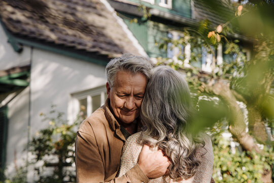 Senior man hugging his wife in garden of their home in autumn