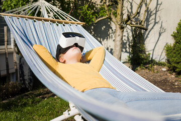 Girl lying in hammock in garden wearing VR glasses
