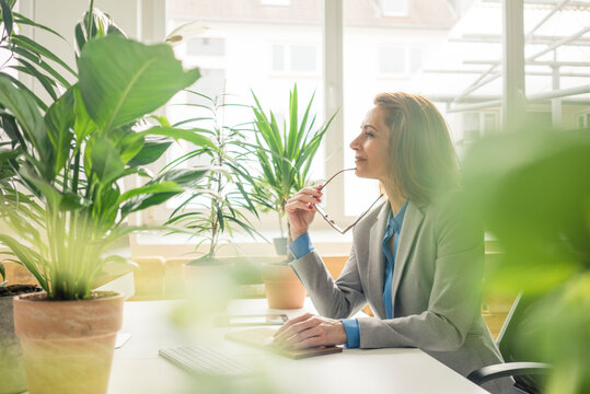Mature businesswoman working in sustainable office, with plants on her desk