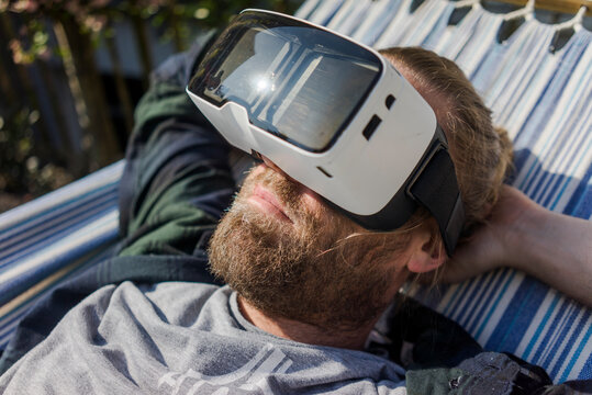 Man lying in hammock in garden wearing VR glasses