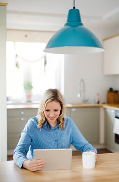 Smiling woman with tablet sitting at table at home