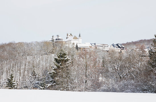 Germany, North Rhine-Westphalia, Hellenthal, Snow-covered forest in front of rural village with&Ocirc;&oslash;&Omega;Wildenburg Castle in background
