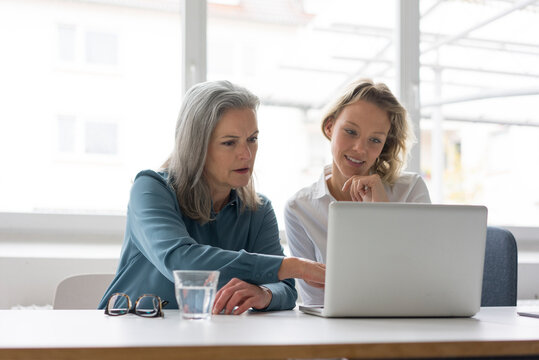 Two businesswomen using laptop at desk in office together