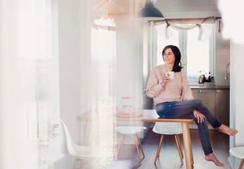 Mature woman sitting on kitchen table, drinking coffee