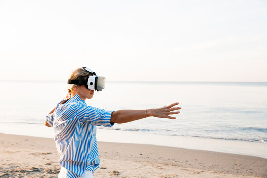 Blonde woman doing kind of yoga exercises on a beach in thailand with 3D virtual reality goggles