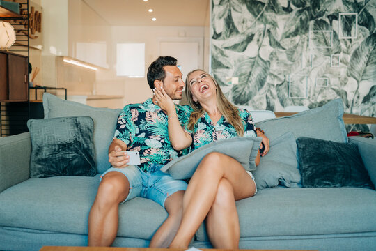 Happy couple sitting on couch in living room wearing Hawaiian shirts