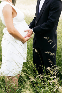 Pregnant bride with her husband holding baby belly on a meadow