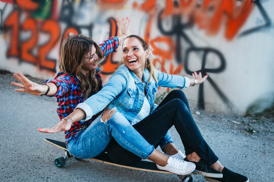 Two laughing friends sitting on longboard with arms outstretched