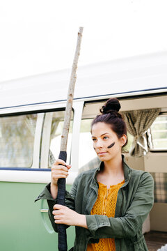 Young woman with spear and facepaint in front of her camper