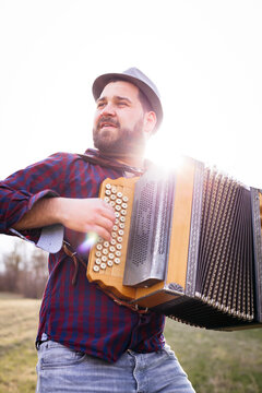 Portrait of bearded man playing accordion on a meadow at backlight