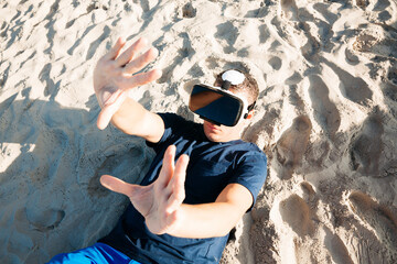Man wearing VR glasses lying in sand on the beach
