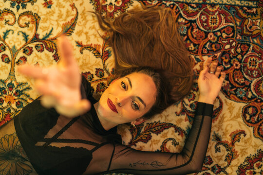 Portrait Of Tattooed Young Woman Lying On The Floor Raising Her Hand