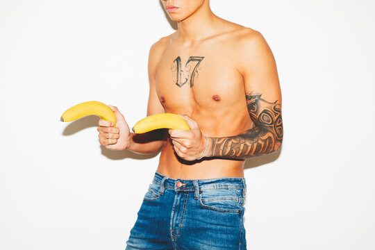 Semi-dressed young man playing with bananas like guns