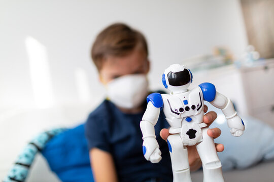Boy with mask playing in his room during the corona crisis with his new, only friend, a robot