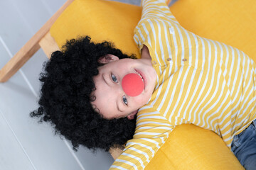 Boy with red clown nose and black hair on yellow couch