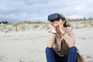 Spain, Menorca, senior woman using VR glasses on the beach in winter