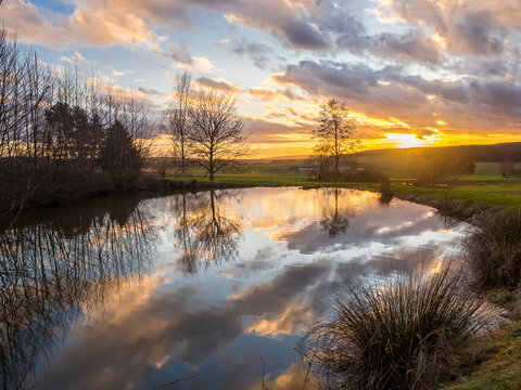 Germany, Bavaria, Clouds reflecting on surface of shiny pond in&Ocirc;&oslash;&Omega;Upper Palatinate Forest at sunset