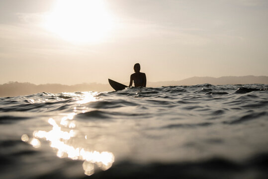 Female surfer sitting on surfboard in the evening, Costa Rica