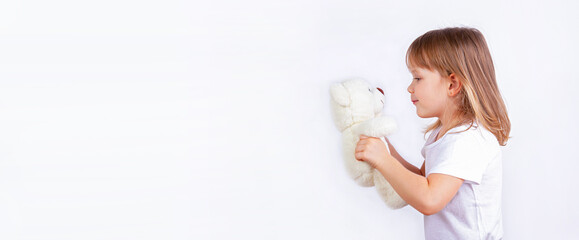 A funny little girl holds her favorite teddy bear in her hands and looks at it.