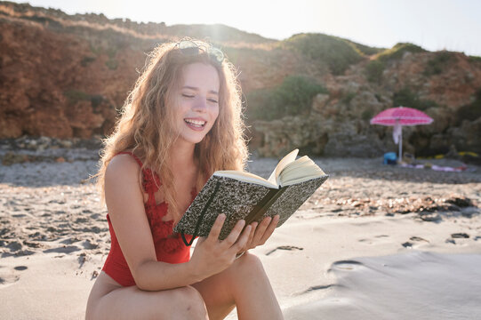 Happy young woman reading book on the beach
