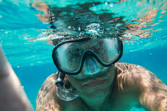 Portrait of man with diving goggles and snorkel taking selfie under water