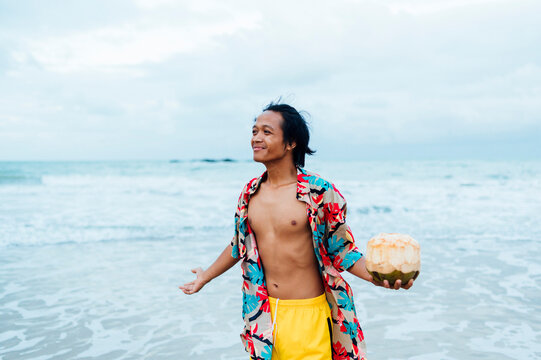 Portrait of happy man with fresh coconut standing in front of the sea, Borneo Island, Malaysia