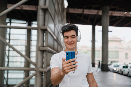 Young man waiting at train station with smartphone and wearing headphones