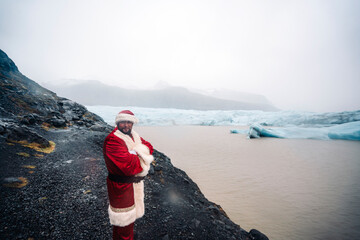 Iceland, smiling Santa Claus standing in front of glacier