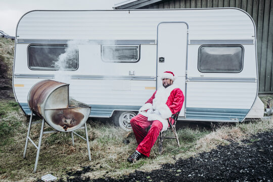 Iceland, Santa Claus sitting in front of caravan barbecueing