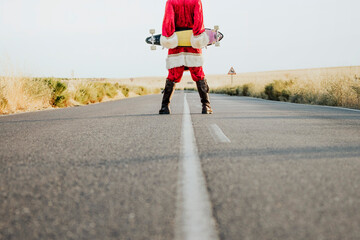Low section of Santa Claus holding a longboard on country road