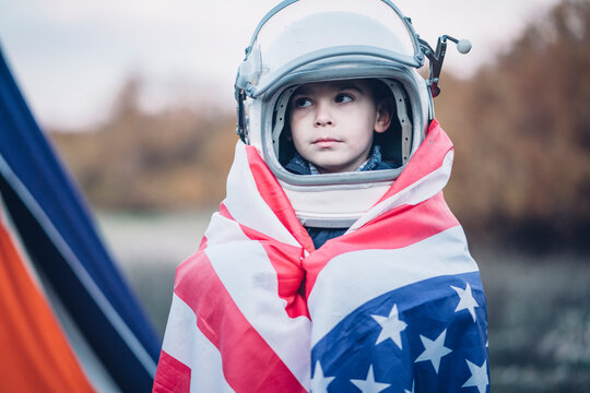 Portrait of little boy wrapped in American flag wearing space helmet
