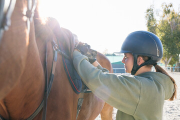 Side view of teenage girl adjusting saddle before riding at training ground