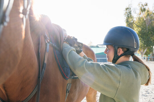 Side view of teenage girl adjusting saddle before riding at training ground